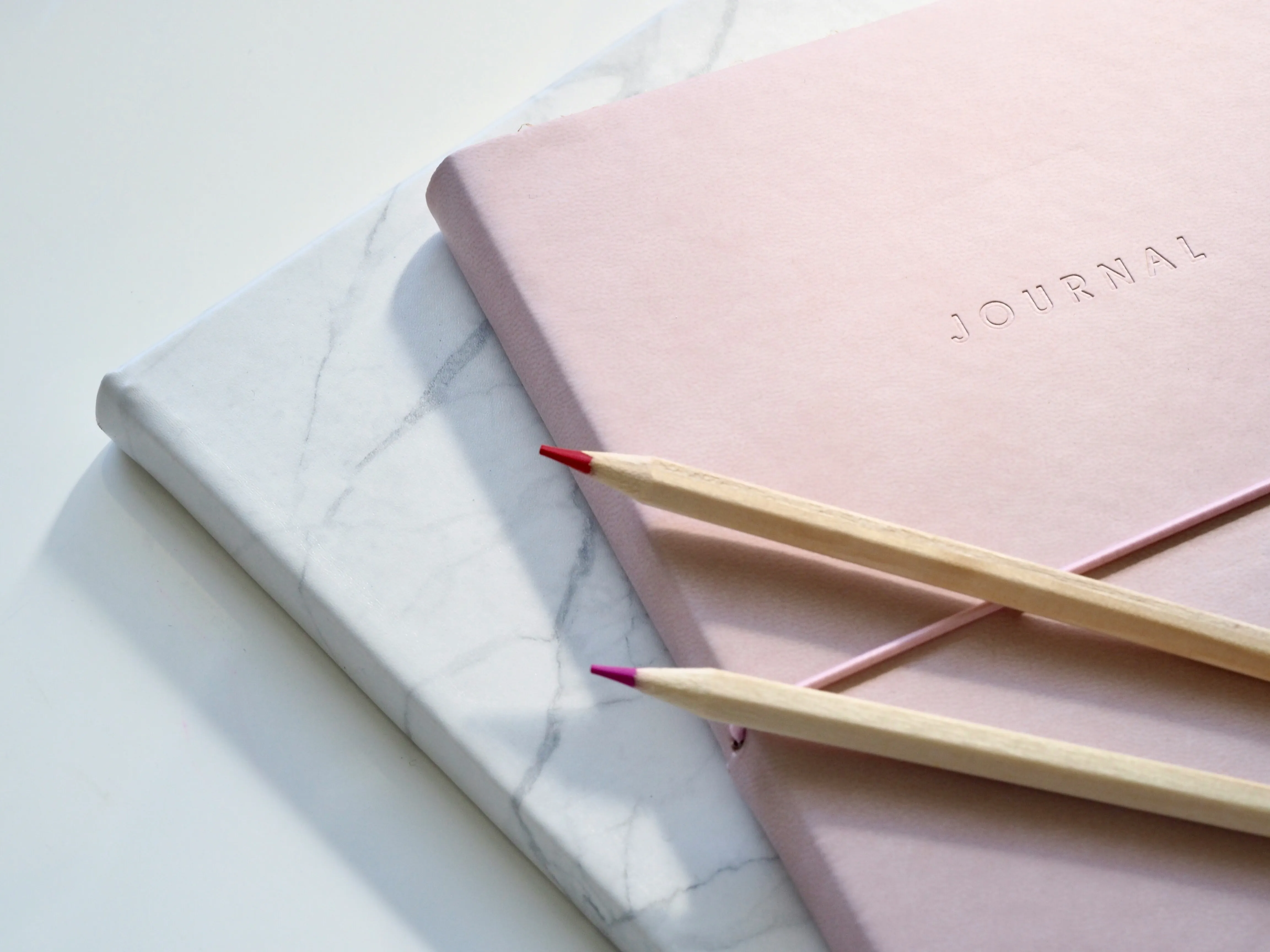 Pink journal and two colored pencils on a marble surface